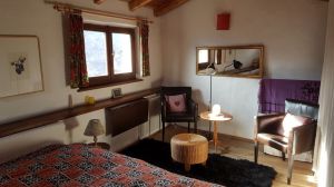 2 Lederstühle, Klappschreibtisch unter Fenster, großer Fernseher abgedeckt neben Gardine. Hinter Gardine rechts: Hochbett, Hängekommode, Treppe nach unten